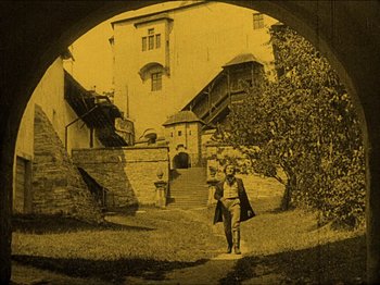 Movie still from “Nosferatu” (1922), directed by F.W. Murnau – A man walking through a tunnel in the middle of a yard; Wide shot, High angle