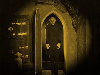 Movie still from “Nosferatu” (1922), directed by F.W. Murnau – A man dressed as a vampire standing in a doorway; Wide shot, High angle