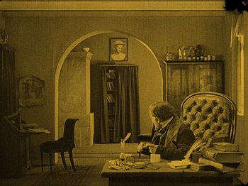 Movie still from “Nosferatu” (1922), directed by F.W. Murnau – An older man sitting in a chair in a living room; Wide shot, High angle
