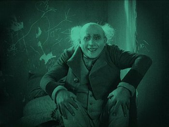 Movie still from “Nosferatu” (1922), directed by F.W. Murnau – An old man with a white wig sitting on a bed; Medium shot, High angle