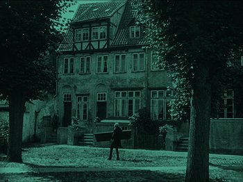Movie still from “Nosferatu” (1922), directed by F.W. Murnau – A person standing in front of an old house; Extreme Wide shot, High angle