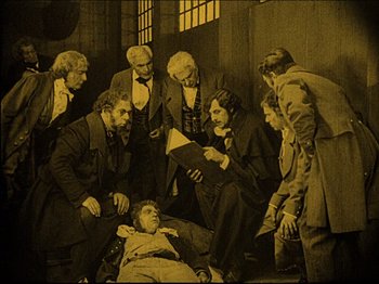 Movie still from “Nosferatu” (1922), directed by F.W. Murnau – A group of men standing around a man laying on the ground; Wide shot, High angle