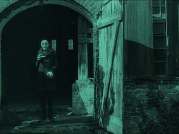 Movie still from “Nosferatu” (1922), directed by F.W. Murnau – A person in a costume standing in front of a door; Wide shot, Low angle