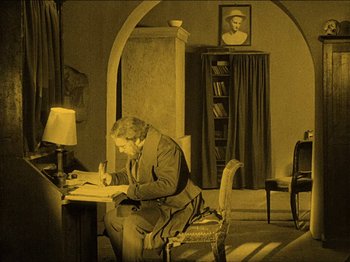 Movie still from “Nosferatu” (1922), directed by F.W. Murnau – A man sitting at a table writing on a piece of paper; Wide shot, High angle