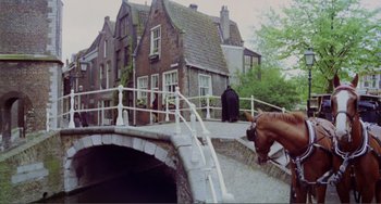 Movie still from “Nosferatu the Vampyre” (1979), directed by Werner Herzog – A person riding a horse over a bridge in front of a house; Extreme Wide shot, Low angle