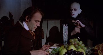 Movie still from “Nosferatu the Vampyre” (1979), directed by Werner Herzog – A man sitting at a dinner table with a bunch of grapes; Medium shot, Over the shoulder angle