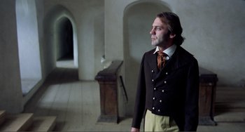 Movie still from “Nosferatu the Vampyre” (1979), directed by Werner Herzog – A man standing in a room wearing a suit and tie; Medium shot, Low angle