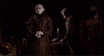 Movie still from “Nosferatu the Vampyre” (1979), directed by Werner Herzog – Two men dressed in dark clothes and one is holding a candle; Medium shot, Low angle