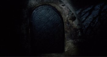 Movie still from “Nosferatu the Vampyre” (1979), directed by Werner Herzog – A dark room with an arched door and a brick wall; Wide shot, High angle