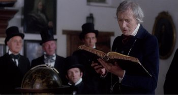 Movie still from “Nosferatu the Vampyre” (1979), directed by Werner Herzog – An old man reading a book in front of a group of men; Medium shot, Low angle