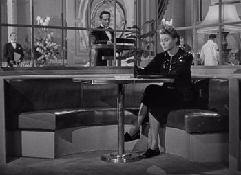 Movie still from “Notorious” (1946), directed by Alfred Hitchcock – A woman sitting at a table in front of a man in a suit; Wide shot, High angle
