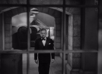 Movie still from “Notorious” (1946), directed by Alfred Hitchcock – A man in a tuxedo standing in front of a jail cell; Wide shot, Over the shoulder angle