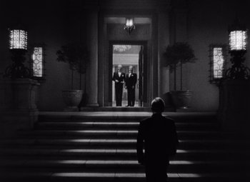Movie still from “Notorious” (1946), directed by Alfred Hitchcock – A man standing on some steps in front of two men; Extreme Wide shot, Low angle