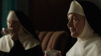 Movie still from “Novitiate” (2017), directed by Maggie Betts – An older woman wearing a nun's hat holding a cup; Close Up shot, Over the shoulder angle