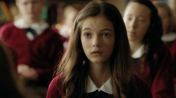 Movie still from “Novitiate” (2017), directed by Maggie Betts – A young girl in a school uniform looking at the camera; Close Up shot, Over the shoulder angle