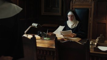 Movie still from “Novitiate” (2017), directed by Maggie Betts – A nun sitting at a desk with papers in her hands; Medium shot, High angle