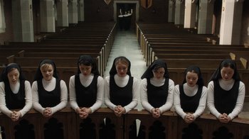 Movie still from “Novitiate” (2017), directed by Maggie Betts – A group of young women standing next to each other in front of pews in a church; Wide shot, High angle