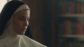 Movie still from “Novitiate” (2017), directed by Maggie Betts – A woman wearing a nun's habit in front of a bookshelf; Close Up shot, Over the shoulder angle