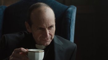 Movie still from “Novitiate” (2017), directed by Maggie Betts – A man in a priest's outfit holding a cup of coffee; Close Up shot, Over the shoulder angle