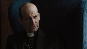 Movie still from “Novitiate” (2017), directed by Maggie Betts – A man in a priest's outfit is looking at the camera; Close Up shot, Over the shoulder angle