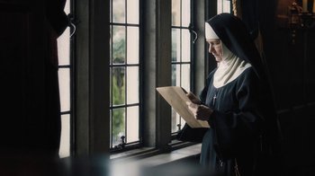 Movie still from “Novitiate” (2017), directed by Maggie Betts – A nun is looking at a piece of paper in front of a window; Medium shot, Low angle