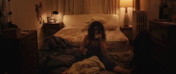 Movie still from “Obvious Child” (2014), directed by Gillian Robespierre – A woman sitting on a bed drinking a beer; Wide shot, High angle