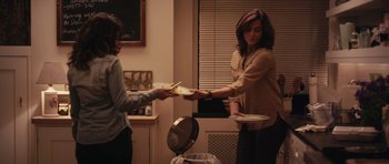 Movie still from “Obvious Child” (2014), directed by Gillian Robespierre – Two women in a kitchen holding plates of food; Medium shot, Over the shoulder angle