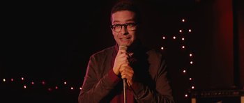 Movie still from “Obvious Child” (2014), directed by Gillian Robespierre – A man holding a microphone and wearing glasses; Close Up shot, Over the shoulder angle