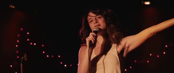 Movie still from “Obvious Child” (2014), directed by Gillian Robespierre – A woman holding a microphone in front of a microphone stand; Medium shot, Low angle