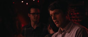 Movie still from “Obvious Child” (2014), directed by Gillian Robespierre – A man standing next to another man in a dark room; Close Up shot, Over the shoulder angle