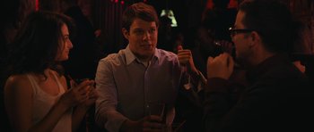 Movie still from “Obvious Child” (2014), directed by Gillian Robespierre – A man holding a glass of wine in his right hand; Medium shot, Over the shoulder angle
