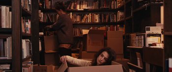 Movie still from “Obvious Child” (2014), directed by Gillian Robespierre – A woman in a box in a room full of books; Medium shot, High angle