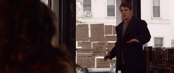 Movie still from “Obvious Child” (2014), directed by Gillian Robespierre – A man standing in front of a store window with a bunch of signs; Medium shot, Over the shoulder angle