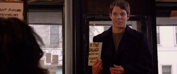Movie still from “Obvious Child” (2014), directed by Gillian Robespierre – A young man holding a book in front of a window; Medium shot, Over the shoulder angle