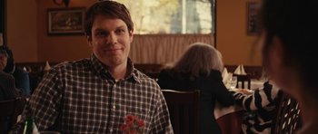 Movie still from “Obvious Child” (2014), directed by Gillian Robespierre – A man sitting at a table holding a bouquet of flowers; Close Up shot, Over the shoulder angle