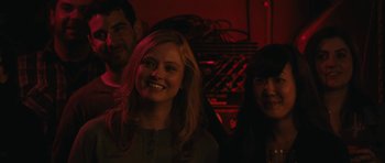 Movie still from “Obvious Child” (2014), directed by Gillian Robespierre – A group of people standing next to each other in a dark room; Close Up shot, Over the shoulder angle