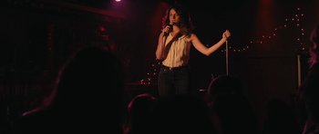 Movie still from “Obvious Child” (2014), directed by Gillian Robespierre – A woman standing on a stage holding a microphone; Medium shot, Over the shoulder angle