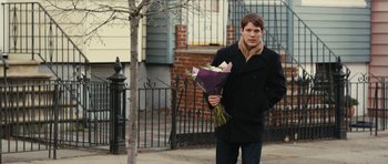 Movie still from “Obvious Child” (2014), directed by Gillian Robespierre – A man holding a bouquet of flowers on the side of the street; Medium shot, Over the shoulder angle