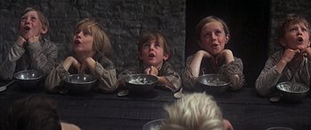 Movie still from “Oliver!” (1968), directed by Carol Reed – A group of young people sitting at a dinner table; Medium shot, Low angle