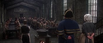 Movie still from “Oliver!” (1968), directed by Carol Reed – A group of people sitting around a table; Wide shot, High angle