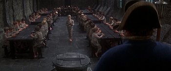 Movie still from “Oliver!” (1968), directed by Carol Reed – A group of people sitting at a long table; Wide shot, High angle