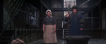 Movie still from “Oliver!” (1968), directed by Carol Reed – A woman standing next to a man holding a cane; Wide shot, Low angle