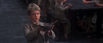 Movie still from “Oliver!” (1968), directed by Carol Reed – A young boy holding a bowl with a spoon in his hand; Medium shot, Low angle