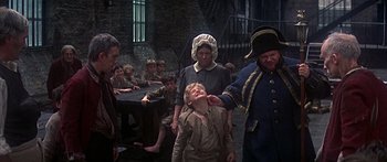 Movie still from “Oliver!” (1968), directed by Carol Reed – A group of people standing around a table; Medium shot, High angle