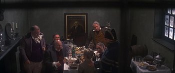 Movie still from “Oliver!” (1968), directed by Carol Reed – A group of people sitting around a table with food on top of it; Wide shot, High angle