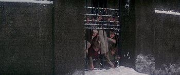 Movie still from “Oliver!” (1968), directed by Carol Reed – A group of children are standing behind a fence; Wide shot, High angle