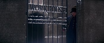 Movie still from “Oliver!” (1968), directed by Carol Reed – A person standing in front of a fence with snow on it; Wide shot, Low angle