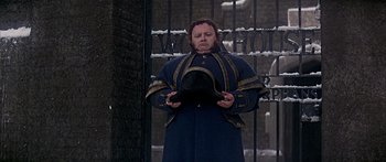 Movie still from “Oliver!” (1968), directed by Carol Reed – A man holding a hat standing in front of a gate; Close Up shot, Low angle