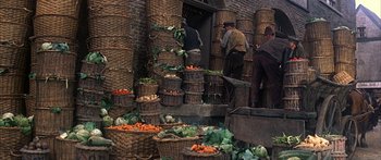 Movie still from “Oliver!” (1968), directed by Carol Reed – A group of people standing around a building filled with lots of baskets of vegetables; Wide shot, High angle
