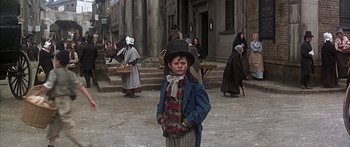 Movie still from “Oliver!” (1968), directed by Carol Reed – A young boy wearing a top hat in the middle of a street; Wide shot, High angle